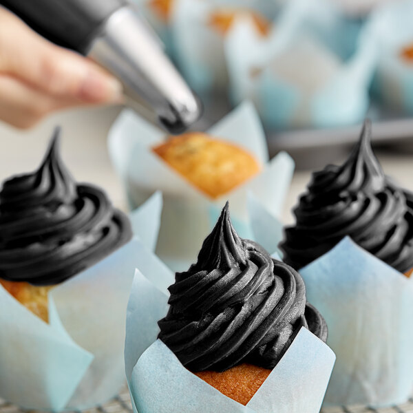A hand using Chefmaster Coal Black gel food coloring to frost a cupcake with black frosting.