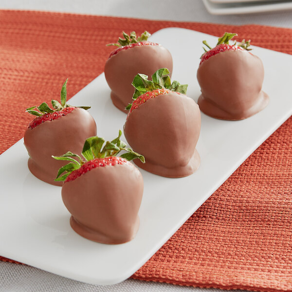 A plate of Ghirardelli milk chocolate covered strawberries with green leaves.