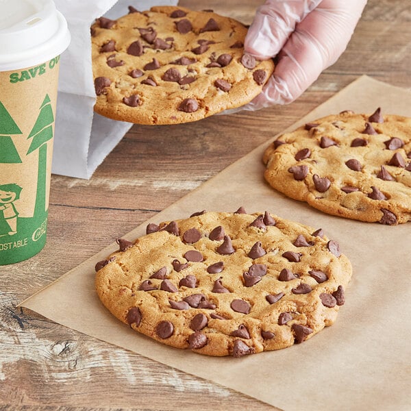 A hand holding a chocolate chip cookie. The cookie is on a table.