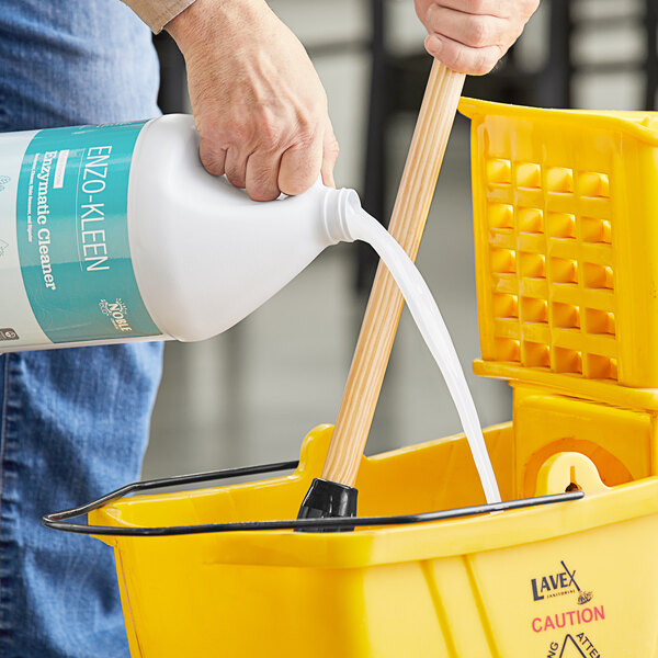 A hand pouring yellow Noble Eco Enzo-Kleen multi-purpose cleaner into a white bucket.
