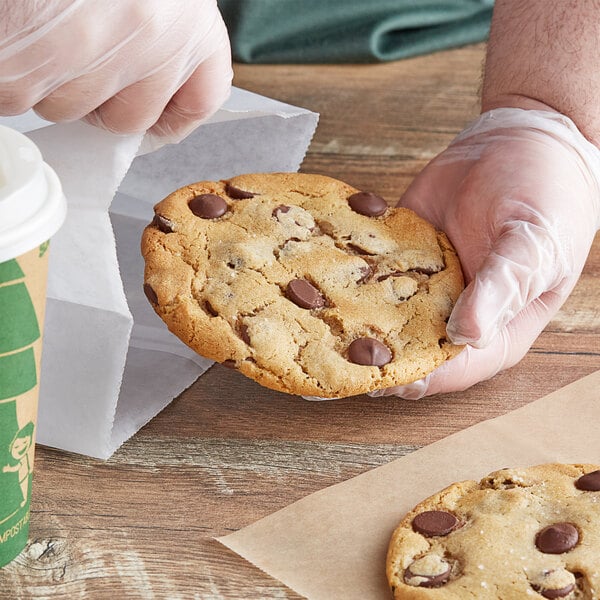 A hand in a plastic glove putting a Ghirardelli 60% Cacao Dark Chocolate baking chip cookie into a bag.