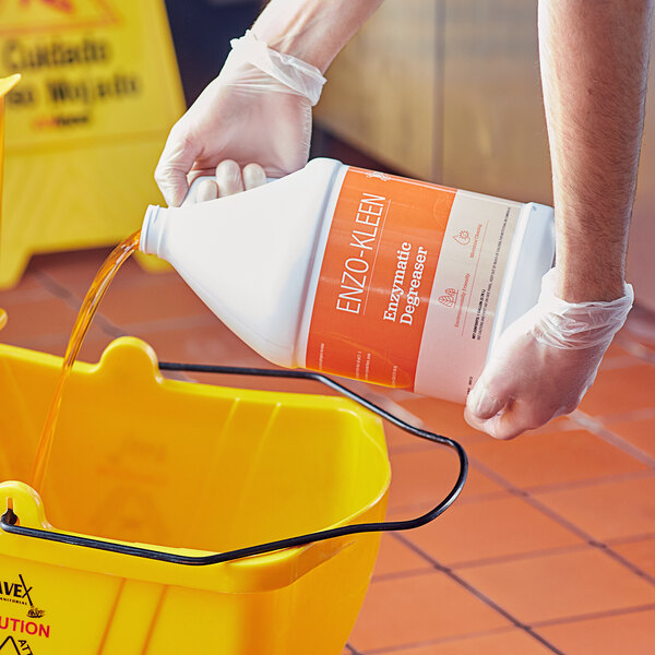 A person in gloves pouring Noble Eco Enzo-Kleen into a yellow bucket.