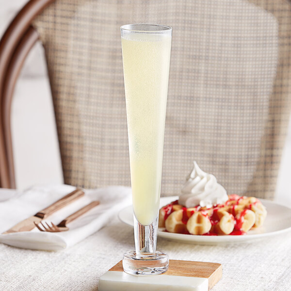 A Fortessa Temptationz flute glass of lemonade with a straw sits on a table.