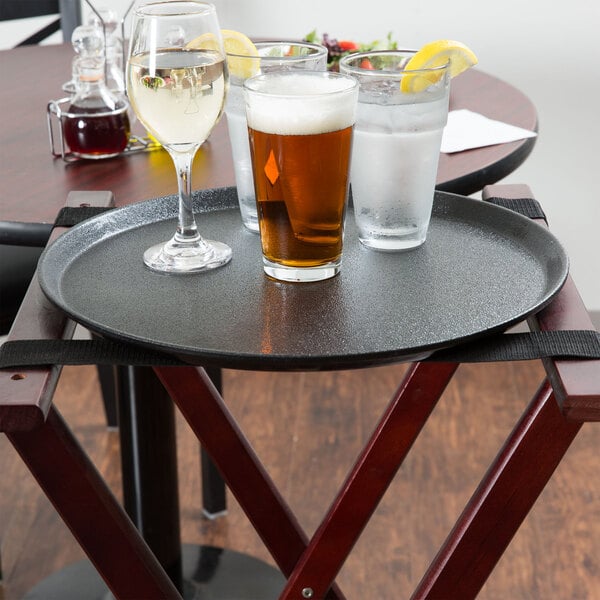 A Carlisle black non-skid fiberglass serving tray holding two glasses of beer and a glass of white wine on a table.
