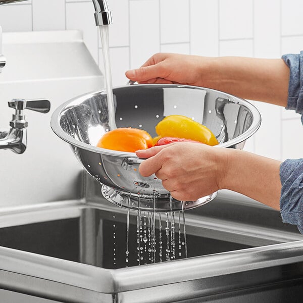 A person washing vegetables in a Choice stainless steel colander.