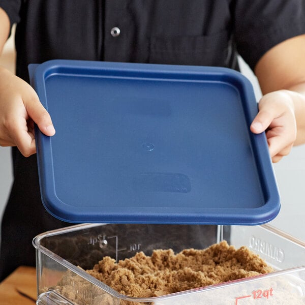 A person holding a blue lid over a Cambro blue plastic food storage container.