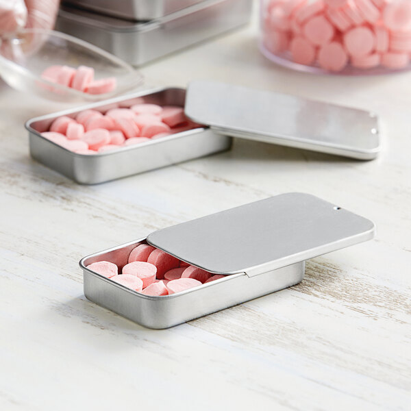 A silver medium metal tin with a slide top filled with pink pills.