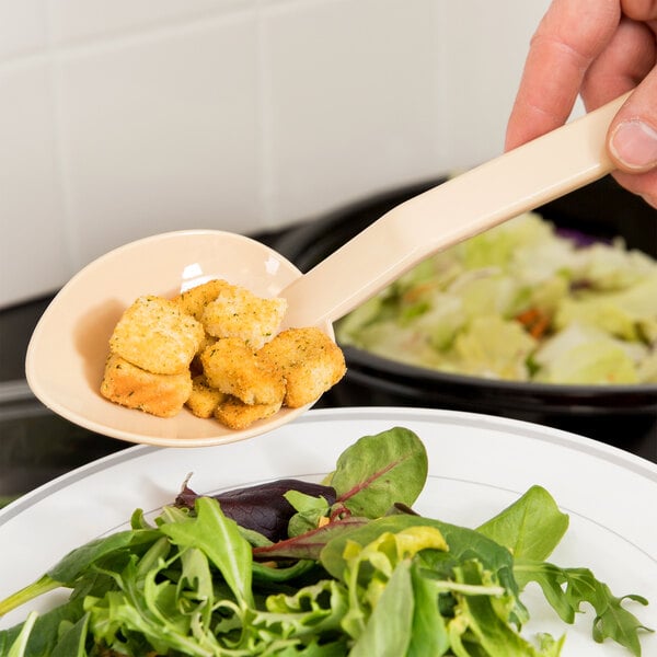 A person using a Thunder Group Beige Polycarbonate salad bar spoon to serve croutons over a bowl of salad.