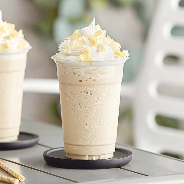 A close up of two white milkshakes with whipped cream and straws.