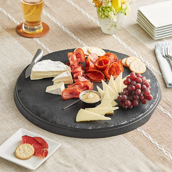 An Acopa faux slate tray with cheese, grapes, and crackers on a table.
