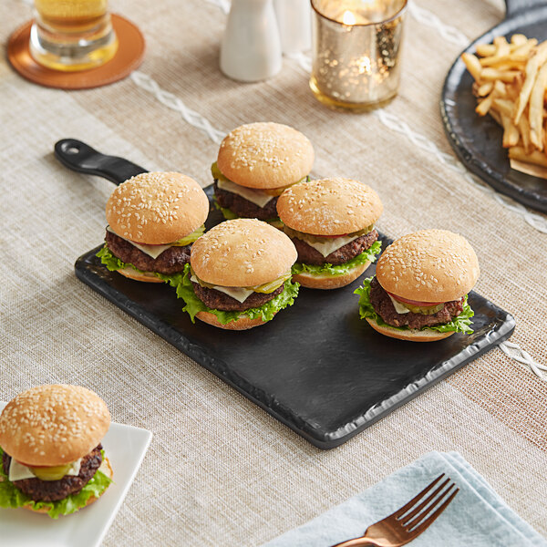 An Acopa faux slate melamine serving board with four hamburgers and a glass of beer on it.