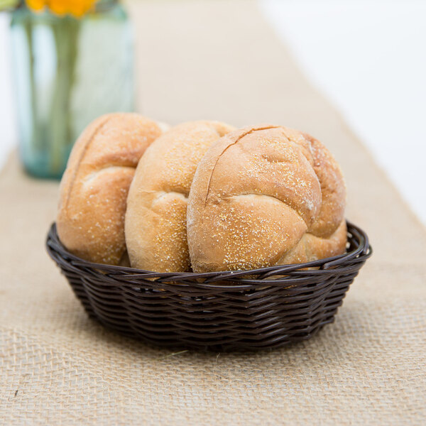 A Tablecraft brown rattan bread basket filled with bread on a table.