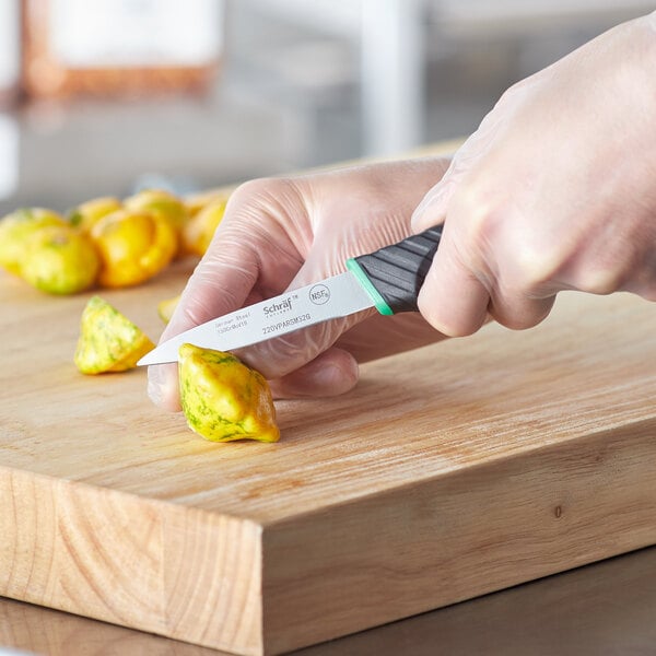 A hand using a Schraf smooth edge paring knife with a white blade to cut a yellow pepper on a cutting board.