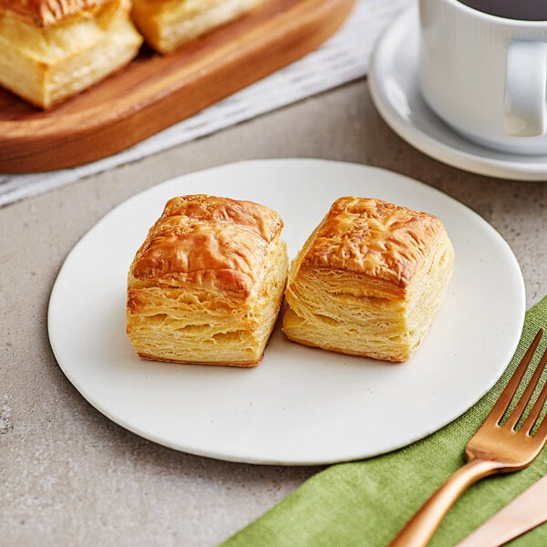 Two Orange Bakery butter flake pastry rolls on a plate with a fork and a white mug of coffee.