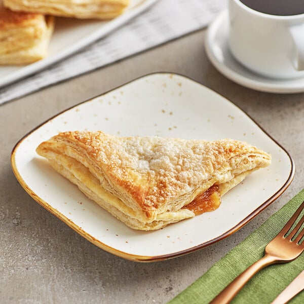 A plate with an Orange Bakery sugared apple turnover on it next to a cup of coffee.