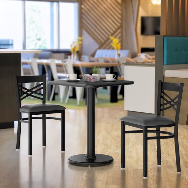A Lancaster Table & Seating reversible cherry and black laminated table top on a black table base with chairs around it.