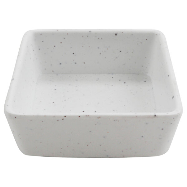 A white square bowl with black specks.