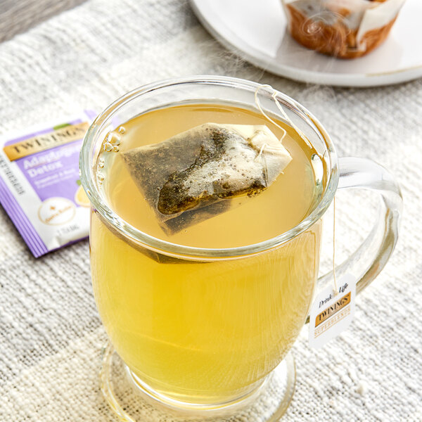 A glass mug of Twinings Detox Adaptogens Grapefruit & Basil Green Tea with a tea bag in it.