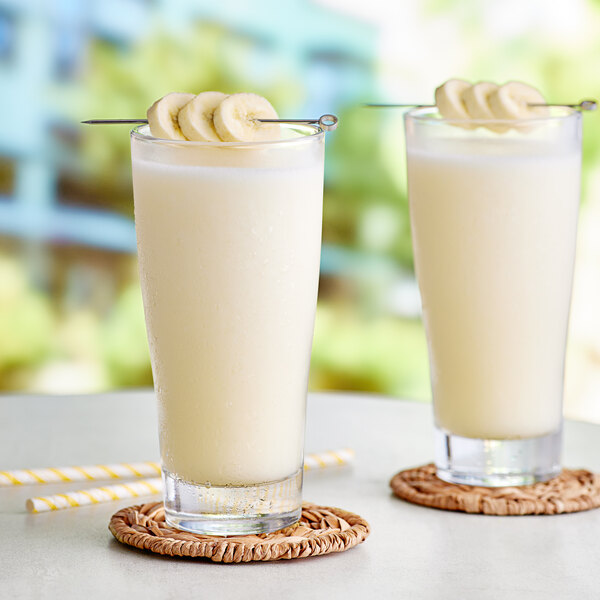 Two glasses of Capora banana smoothie with bananas on top.