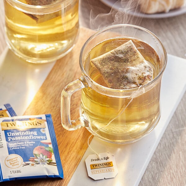 A glass mug of Twinings Unwind Passionflower & Chamomile, Spiced Apple & Vanilla Herbal Tea with a tea bag in it.