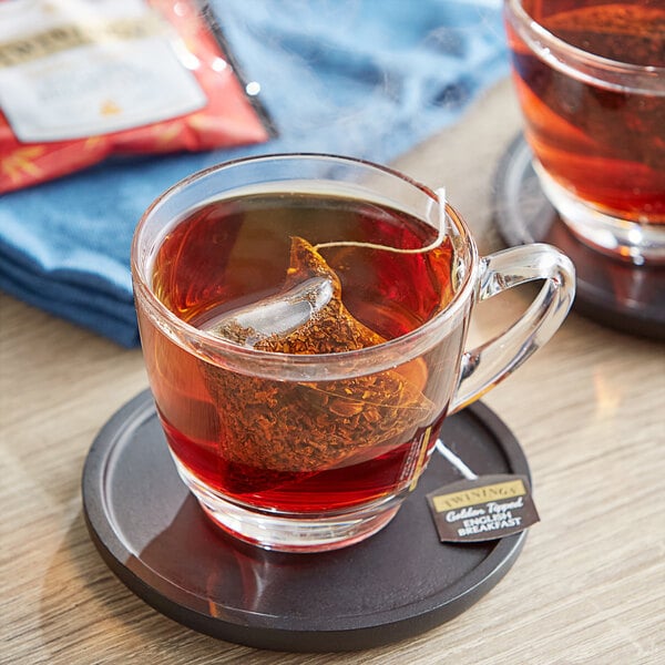 A glass of Twinings English Breakfast tea on a coaster with a tea bag in it.