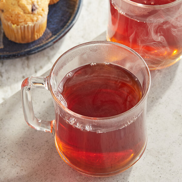 A glass mug of Twinings English Breakfast Tea with a plate of muffins on the table.