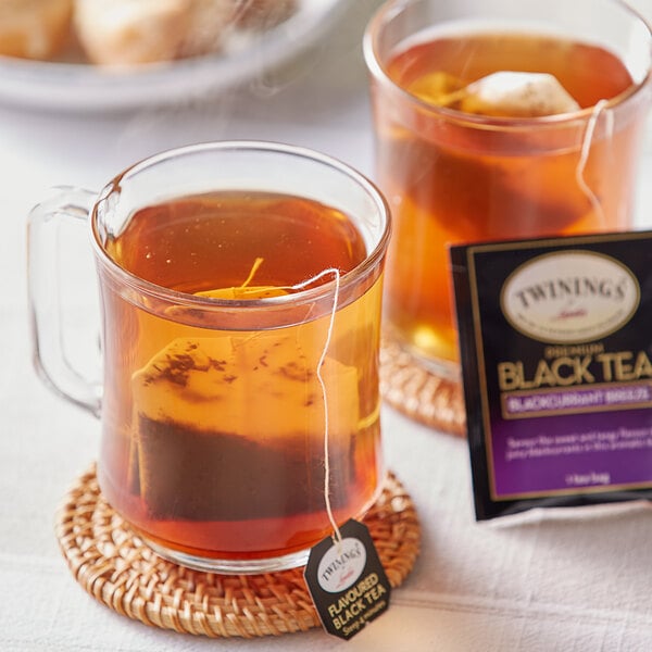 A glass mug of Twinings Blackcurrant Breeze tea with a tea bag in it.