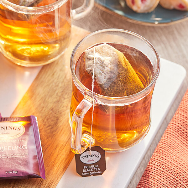 A glass mug of Twinings Darjeeling tea with a tea bag in it.