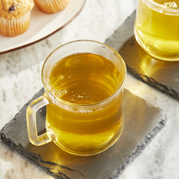 Two Twinings Green Decaffeinated Tea K-Cups in glass mugs on a stone coaster with muffins.