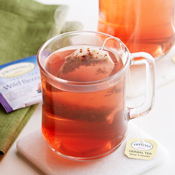 A glass mug of Twinings Wild Berries herbal tea with a tea bag in it.