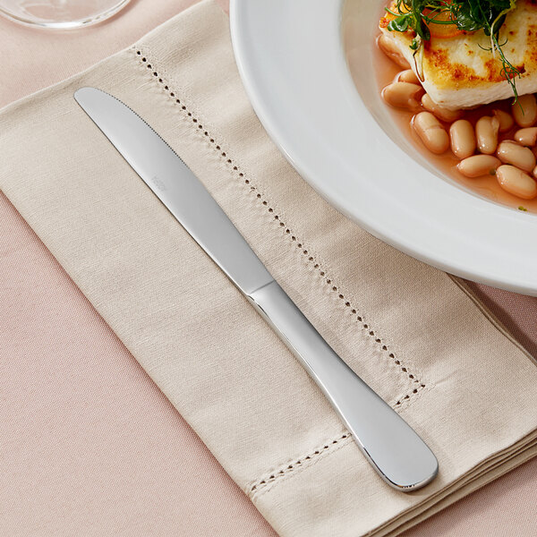An Acopa Triumph stainless steel dinner knife on a napkin next to a plate of food with beans.