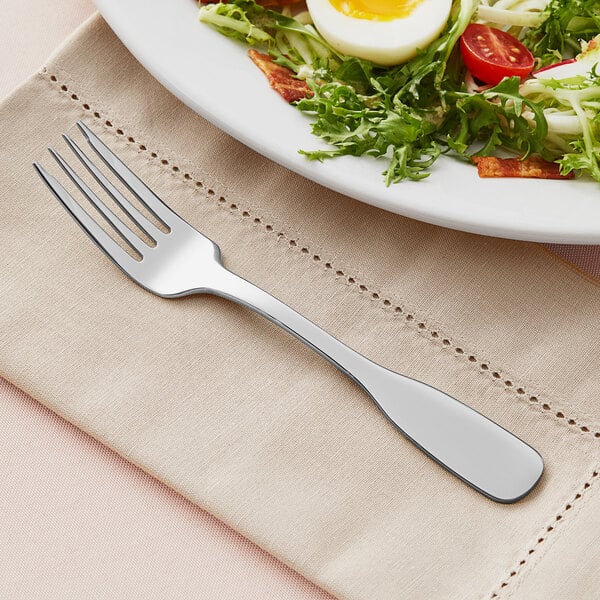 An Acopa Triumph stainless steel salad fork with salad on a plate.