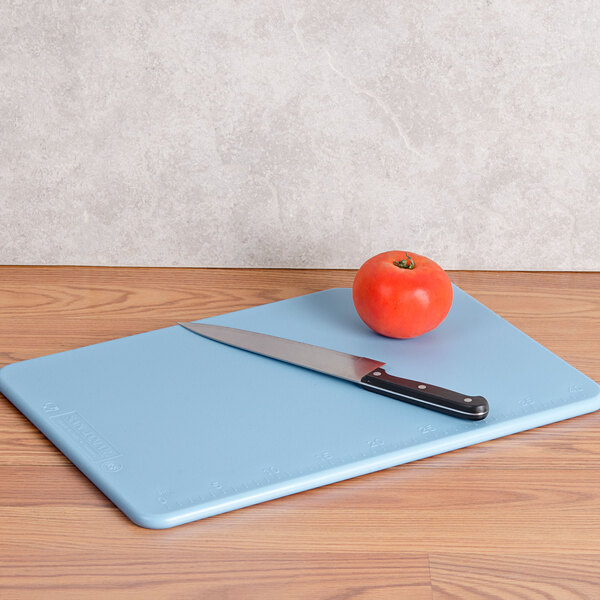 A San Jamar blue cutting board with a knife and tomato on it.