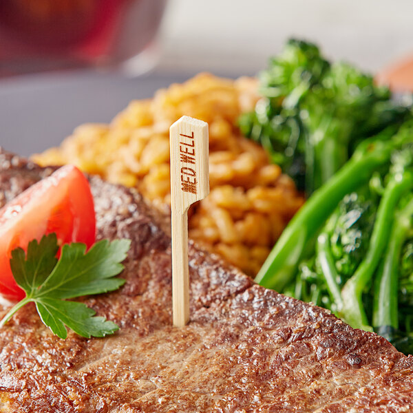 A steak with a Tablecraft bamboo "Medium Well" marker on a plate with broccoli.