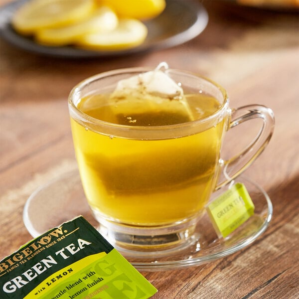 A glass cup of Bigelow Green Tea with Lemon with a tea bag in it.