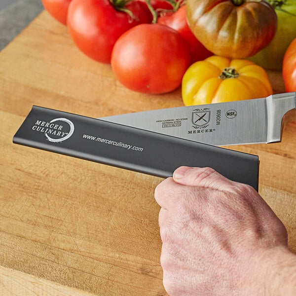 A person holding a Mercer Culinary knife with a yellow vegetable being cut.