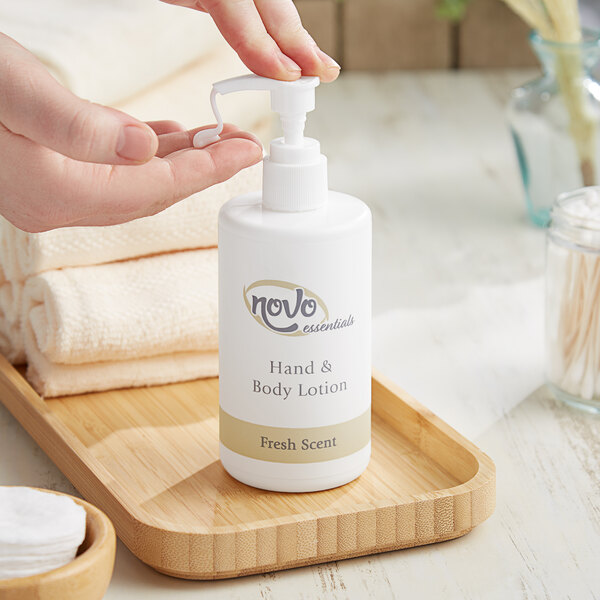 A hand holding a white pump bottle of Novo Essentials Hotel and Motel Hand and Body Lotion.