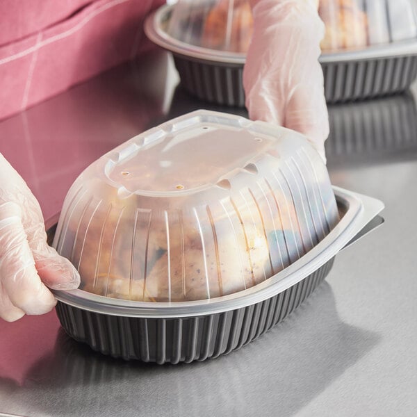A person in a plastic glove holding a D&W Fine Pack black plastic container with food and a dome lid.