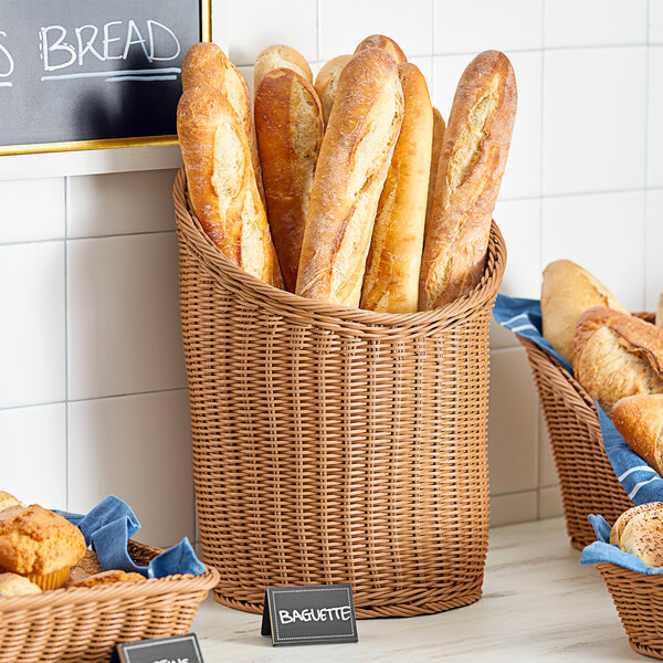 An Acopa dark brown woven plastic rattan basket filled with loaves of bread.