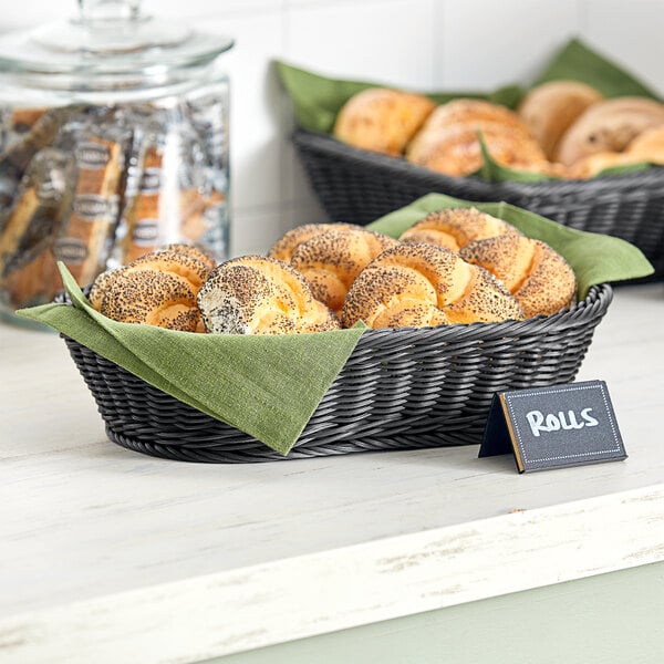 An Acopa black plastic woven basket filled with rolls on a bakery counter.