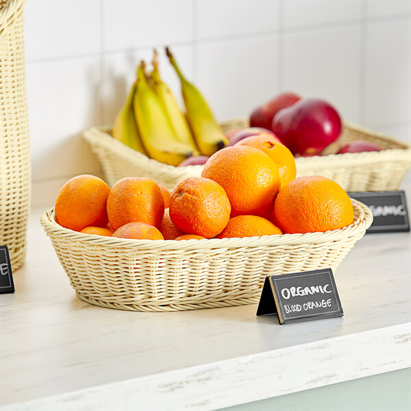 An Acopa woven plastic rattan basket with oranges and bananas on a hotel buffet counter.
