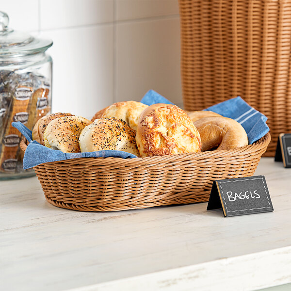 An Acopa dark brown woven plastic rattan basket filled with bagels and other food items on a bakery counter.