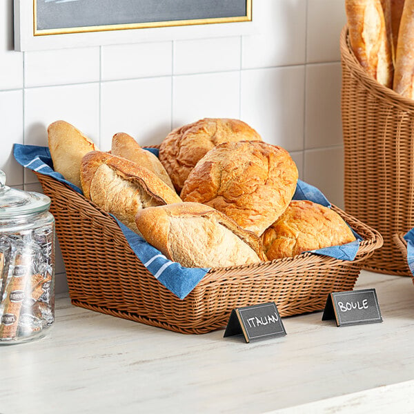 A slanted dark brown woven plastic rattan basket holding a loaf of bread on a bakery display counter.