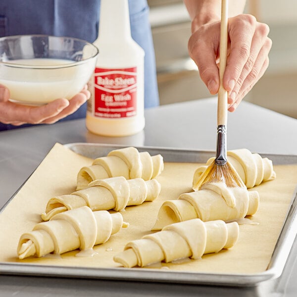 A person using Bake Sheen liquid to brush pastries before baking.