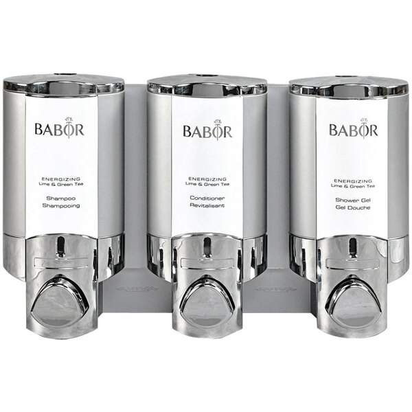 A room with a chrome Dispenser Amenities wall mounted soap dispenser with three satin silver Babor bottles.