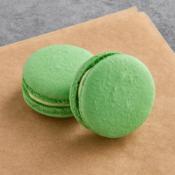 Two green Macaron Centrale macarons on a brown surface.