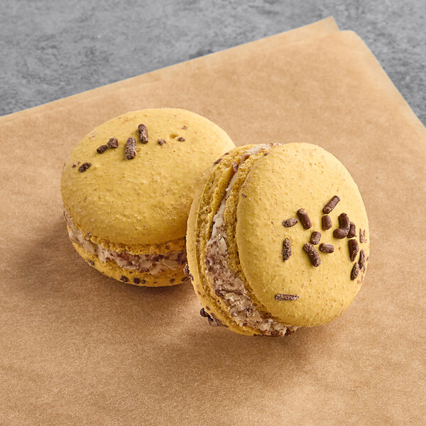Two yellow macarons with chocolate chips on a paper.