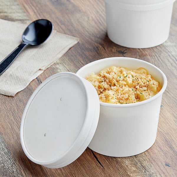 A white container of food with a vented paper lid on a table.