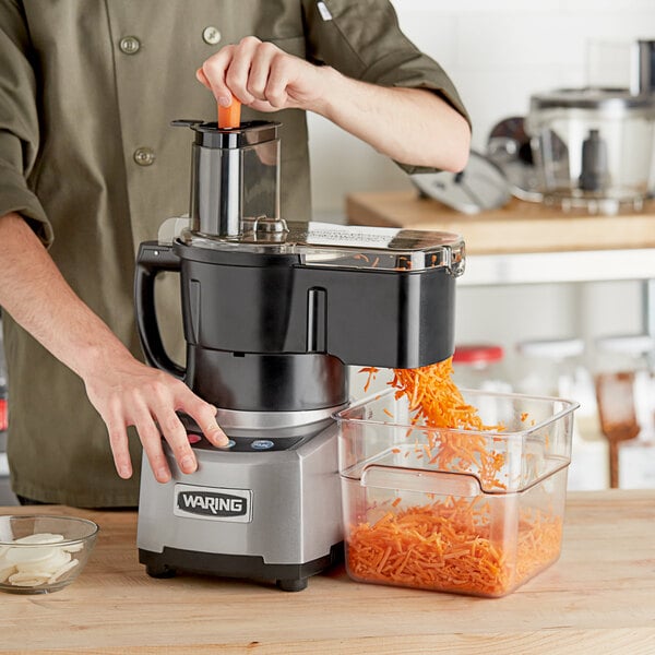 A person using a Waring food processor to shred carrots into a container.