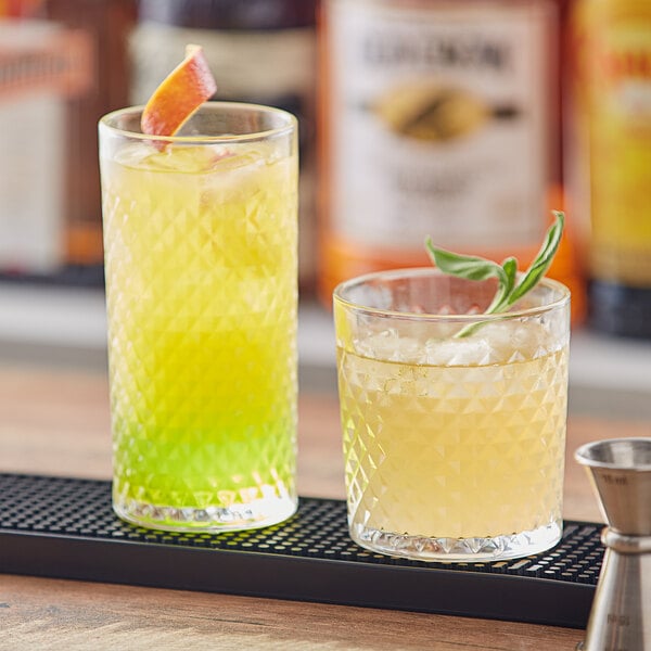 Two Acopa Aurelius cocktail glasses filled with yellow and green drinks on a bar counter.